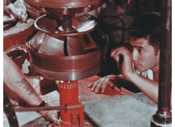 Man looks at broken nuclear recirculation pump while trying to fix it. It is jacked up on a red jack.