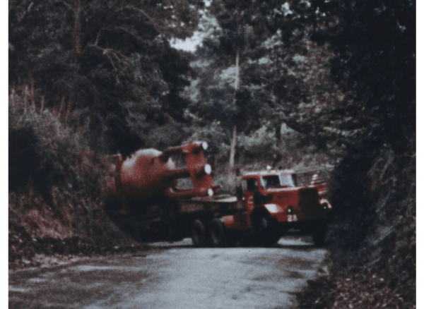 Truck carrying BONUS vessel gets stuck in a tight forested corner on the street. It is basically pinned as it tries to round the corner.