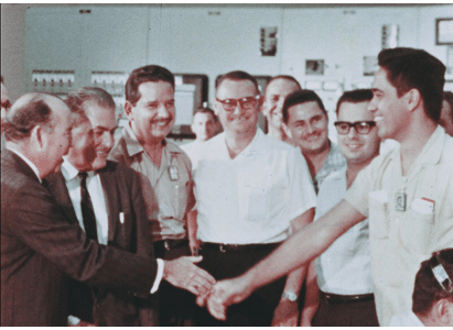 11 smiling men shaking hands in the control room of bonus after achieving initial criticality.