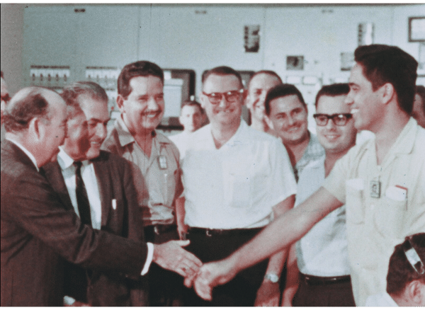 11 smiling men shaking hands in the control room of bonus after achieving initial criticality.