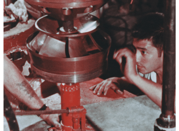 Man looks at broken nuclear recirculation pump while trying to fix it. It is jacked up on a red jack.