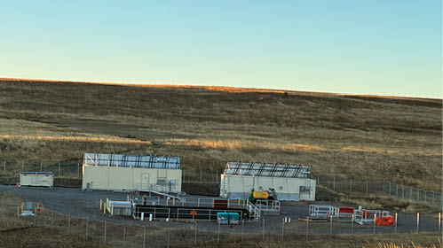 A view of a field with a fence and a building in the background. AI generated content